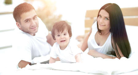 Happy young family with a baby lying in bed and smilingの写真素材