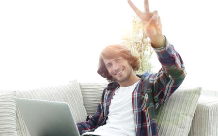 happy guy with laptop sitting on sofa and showing his hand a winの写真素材