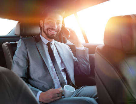 businessman sitting in car with cup and smartphoneの写真素材