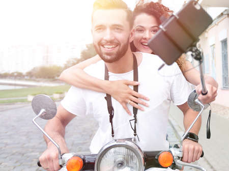 Happy couple on scooter making selfie on smartphone outdoor