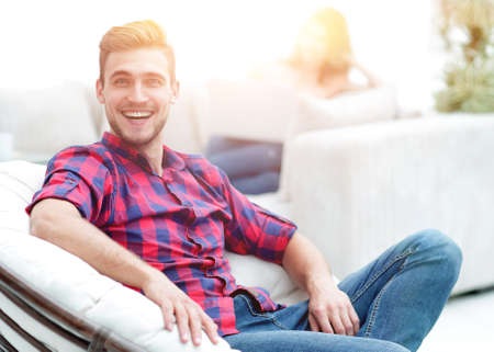 happy young man sitting in a big chair on blurred backgroundの写真素材