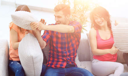 group of friends playing pillow fight, sitting on the couchの写真素材