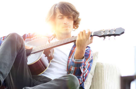 Handsome man playing on the guitar on the couch at home