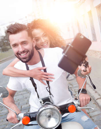 Happy couple on scooter making selfie on smartphone outdoor