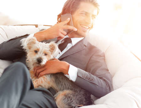 successful businessman holds his dog and pet and talks on the smartphoneの写真素材