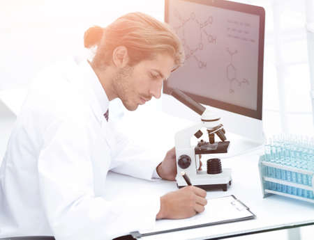 Laboratory worker sitting by table with microscopeの写真素材