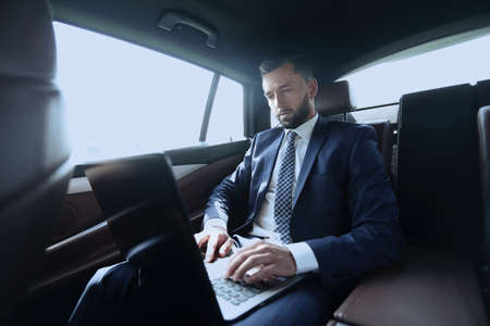 businessman sitting in the back-seat of a car, using his laptop