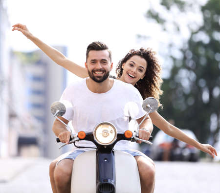 Happy young couple riding a scooter in the city on a sunny dayの写真素材