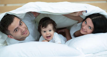 Happy family posing under a duvet while looking at the camera