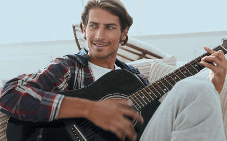 modern guy with guitar sitting on sofa in living room.