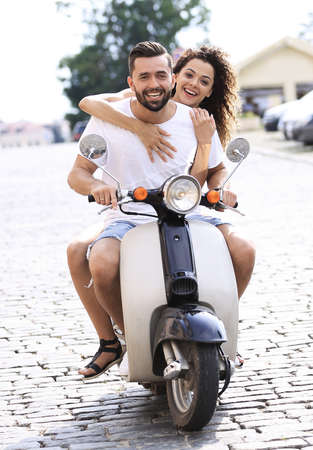 Happy young couple riding a scooter in the city on a sunny dayの写真素材