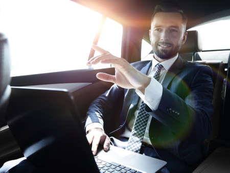 businessman sitting in the back seat in the car and pointing his finger forwardの写真素材