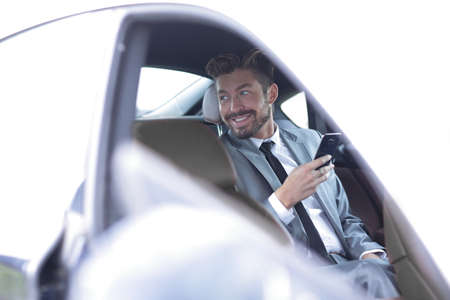 Unsmiling businessman sitting in the back seat in his car