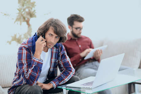 guy with a friend sitting on the couch, talking on the smartphone and searching for information on the Internet.の写真素材