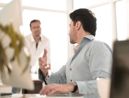 business man talking to a colleague sitting at his Desk