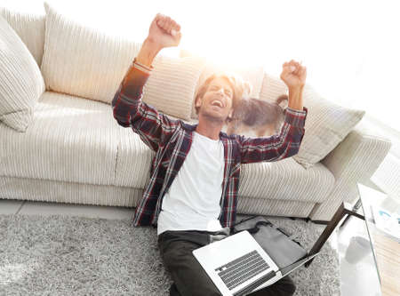 happy guy with laptop jubilant in spacious living room.の写真素材