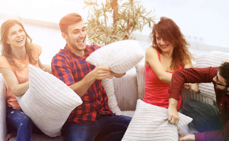 cheerful friends playing pillow fight, sitting on the couchの写真素材