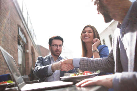handshake colleagues at a table in a street cafe