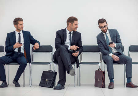 employees with smartphones sitting in the office hallwayの写真素材
