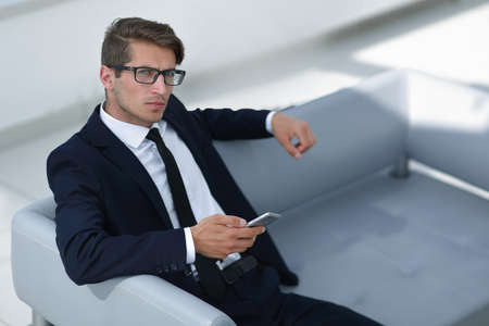 serious businessman with mobile sitting in the office lobby