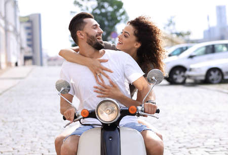 Happy young couple riding a scooter in the city on a sunny day