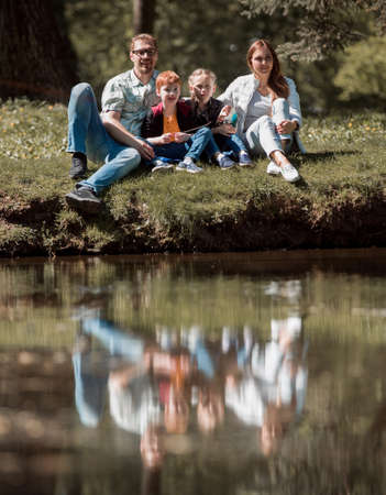 happy family of four sitting on the grass on the lakeの写真素材