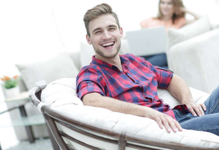 happy young man sitting in a big chair on blurred backgroundの写真素材