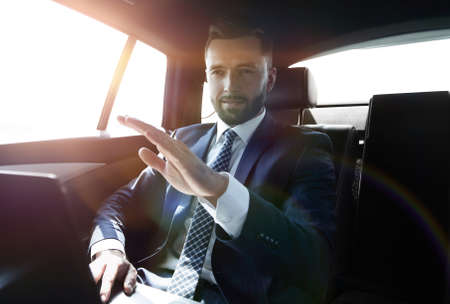 businessman sitting in the back seat in the car and pointing his finger forwardの写真素材