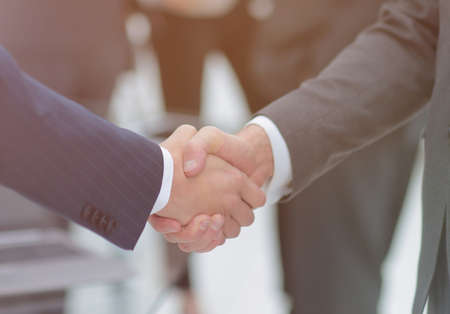 Two businessmen shaking hands with colleagues  on background.