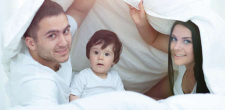 Families with children in bed under a blanketの写真素材