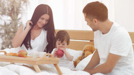 Family taking the breakfast on the bed in the bedroomの写真素材
