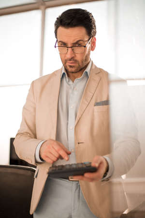 serious businessman using a calculator while standing in the empty officeの写真素材