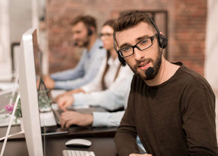 man with headset sitting by computers in a bright office