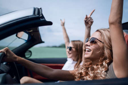 happy young women driving in in cabriolet car and laughingの写真素材