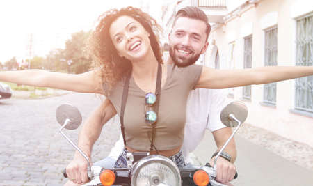 Beautiful young couple is smiling while riding a scooterの写真素材