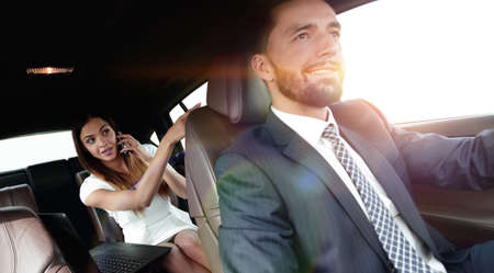 Young businesswoman with laptop on back seat in carの写真素材