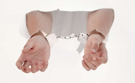 Handcuffs on the hands of a man breaking a paper wall
