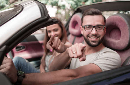 loving couple in a convertible car pointing at you