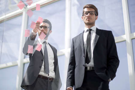 Business colleagues read stickers pasted on a transparent glass wall.の写真素材