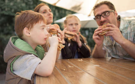 happy family eating burgers sitting at a table in a cafeの写真素材