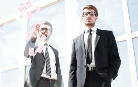 Business colleagues read stickers pasted on a transparent glass wall.の写真素材