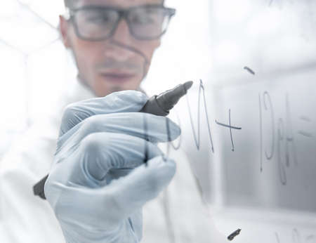 young scientist writes a formula on a glass Board