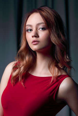 Charming brunette in a red dress posing on a black background.の写真素材