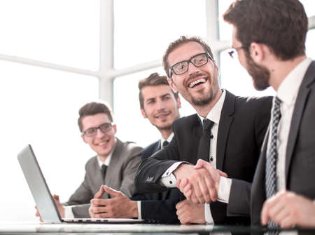 colleagues shaking hands while sitting at their Desk.の写真素材