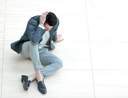 frustrated young businessman sitting on the floor and looking down.の写真素材