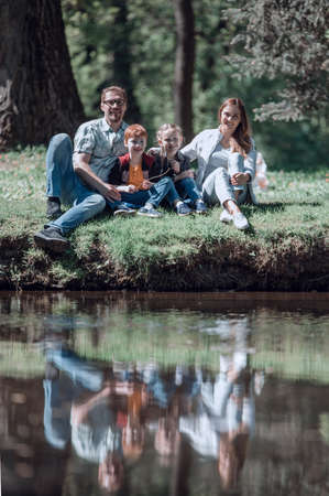happy family of four sitting on the grass on the lakeの写真素材