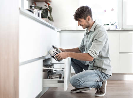 young man looking at clean dishes in dishwasherの写真素材