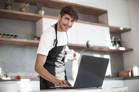 young man looking at laptop screen while cooking dinnerの写真素材