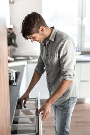 young man opens the built-in refrigerator in his kitchen.の写真素材