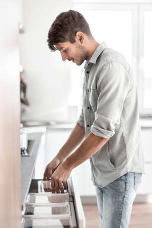 young man opens the built-in refrigerator in his kitchen.の写真素材